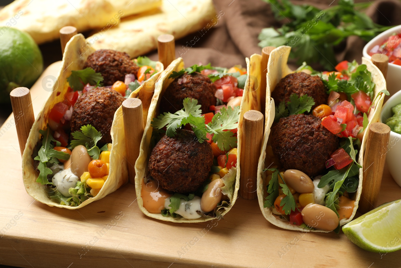 Photo of Tasty vegetarian tacos with falafel served on wooden table, closeup