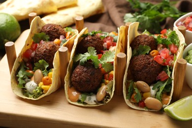 Photo of Tasty vegetarian tacos with falafel served on wooden table, closeup