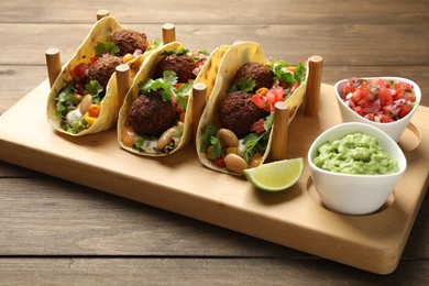 Photo of Tasty vegetarian tacos with falafel served with salsa and guacamole on wooden table, closeup