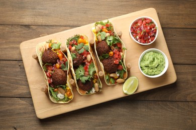 Photo of Tasty vegetarian tacos with falafel served with salsa and guacamole on wooden table, top view