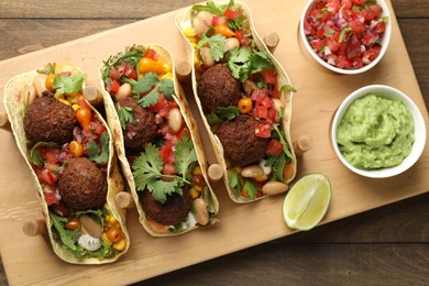 Photo of Tasty vegetarian tacos with falafel served with salsa and guacamole on wooden table, top view