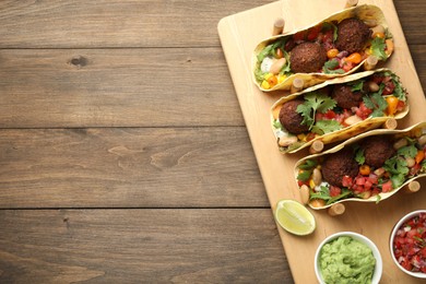 Photo of Tasty vegetarian tacos with falafel served with salsa and guacamole on wooden table, top view. Space for text