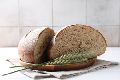 Photo of Pieces of fresh bread and green wheat spikes on white wooden table, closeup