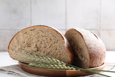Photo of Pieces of fresh bread and green spikes on white table, closeup