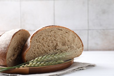 Photo of Pieces of fresh bread and green wheat spikes on white wooden table, closeup