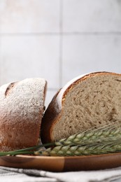 Photo of Pieces of fresh bread and green wheat spikes on table, closeup