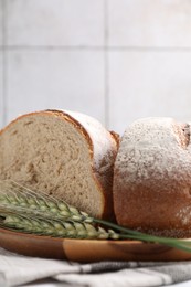 Photo of Pieces of fresh bread and green wheat spikes on table, closeup