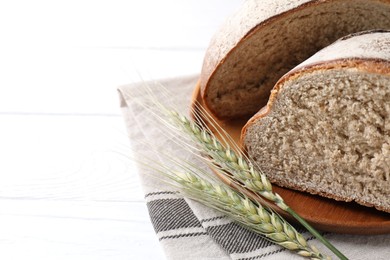 Photo of Pieces of fresh bread and green wheat spikes on white wooden table, closeup