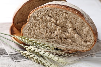Photo of Pieces of fresh bread and green wheat spikes on white table, closeup