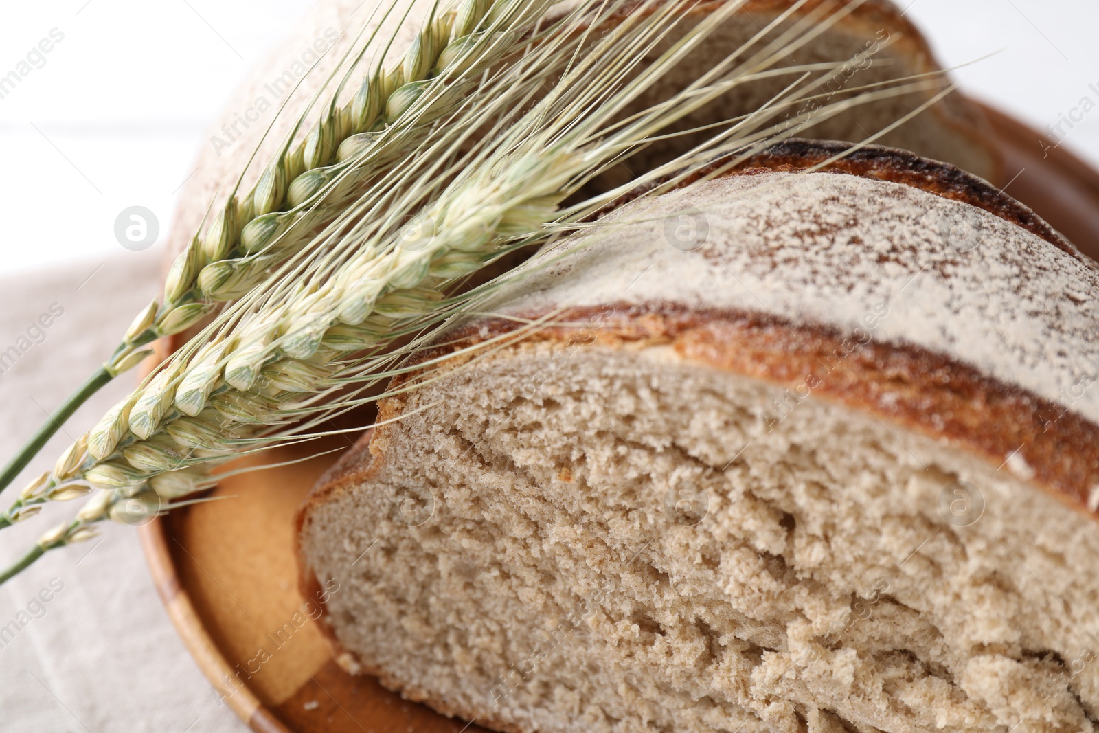 Photo of Pieces of fresh bread and green wheat spikes on white table, closeup