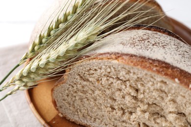 Photo of Pieces of fresh bread and green wheat spikes on white table, closeup