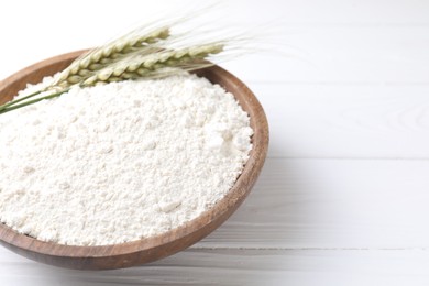 Photo of Flour and green wheat spikes in bowl on white wooden table, closeup. Space for text