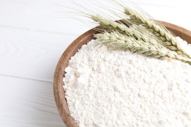 Photo of Flour and green wheat spikes in bowl on white wooden table, closeup