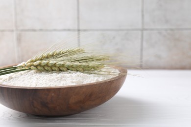 Photo of Flour and green wheat spikes in bowl on white wooden table, closeup. Space for text