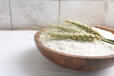 Photo of Flour and green wheat spikes in bowl on white wooden table, closeup. Space for text