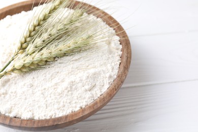 Photo of Flour and green wheat spikes in bowl on white wooden table, closeup. Space for text