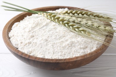 Photo of Flour and green wheat spikes in bowl on white wooden table, closeup