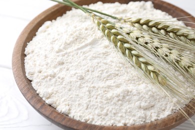 Photo of Flour and green wheat spikes in bowl on white wooden table, closeup