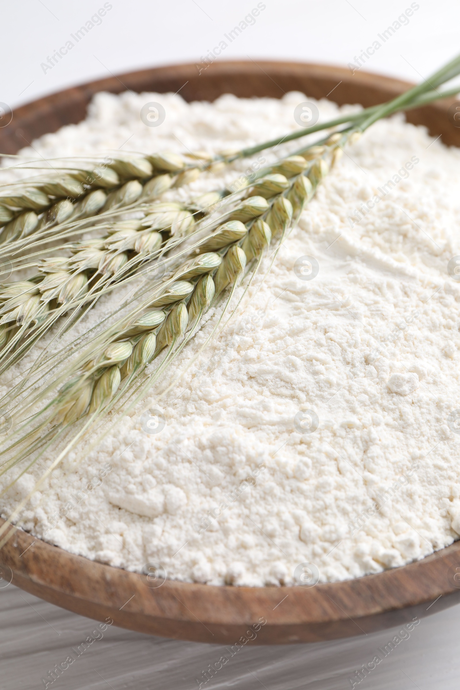 Flour and green wheat spikes in bowl on white wooden table, closeup Photo of Flour and green wheat spikes in bowl on white wooden table, closeup