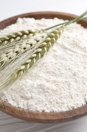 Photo of Flour and green wheat spikes in bowl on white wooden table, closeup