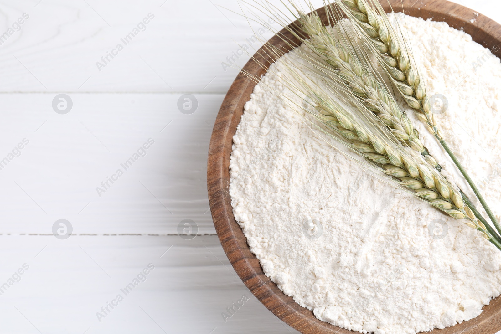 Flour and green wheat spikes in bowl on white wooden table, top view. Space for text Photo of Flour and green wheat spikes in bowl on white wooden table, top view. Space for text