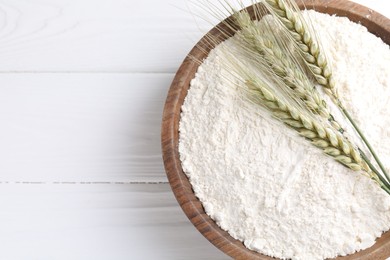 Photo of Flour and green wheat spikes in bowl on white wooden table, top view. Space for text