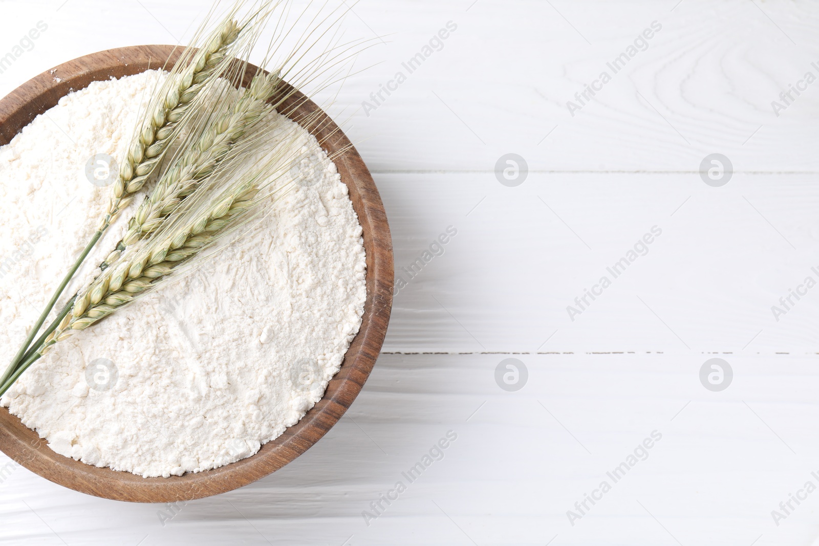 Flour and green wheat spikes in bowl on white wooden table, top view. Space for text Photo of Flour and green wheat spikes in bowl on white wooden table, top view. Space for text