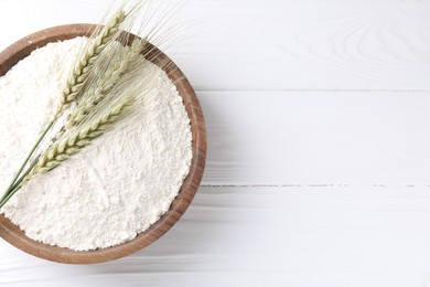 Photo of Flour and green wheat spikes in bowl on white wooden table, top view. Space for text