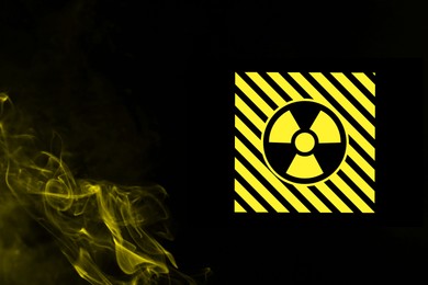 Image of Radioactive sign and yellow toxic smoke against black background