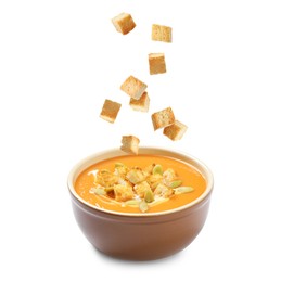 Image of Croutons falling into bowl of creamy pumpkin soup against white background