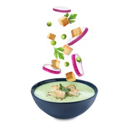 Image of Croutons, onion rings, green peas and parsley falling into bowl of soup against white background