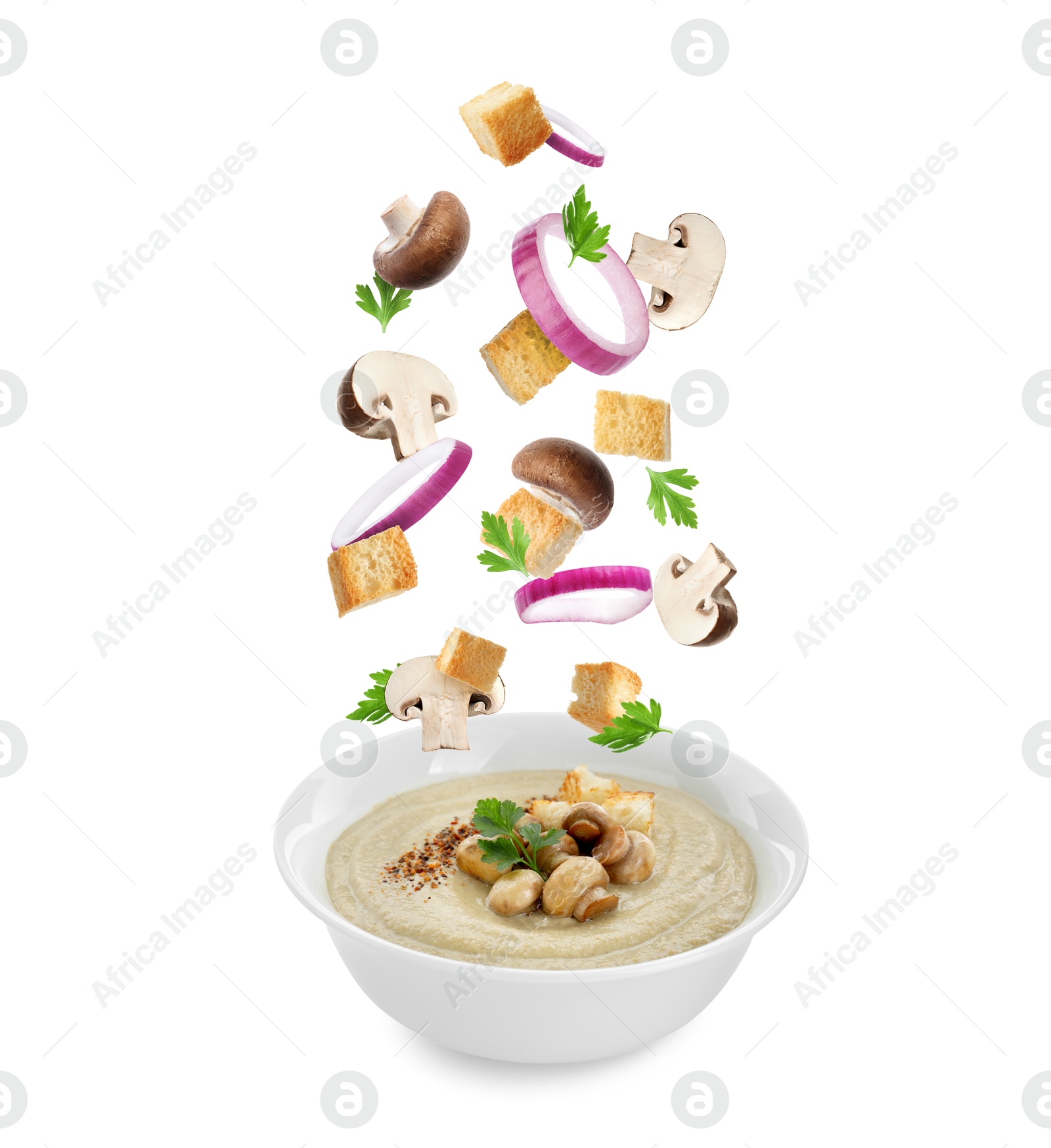 Image of Croutons, onion rings and mushrooms falling into bowl of soup against white background