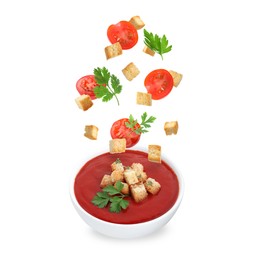 Image of Croutons, tomatoes and parsley falling into bowl of soup against white background