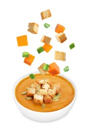 Image of Croutons, green onion and pumpkin cubes falling into bowl of soup against white background