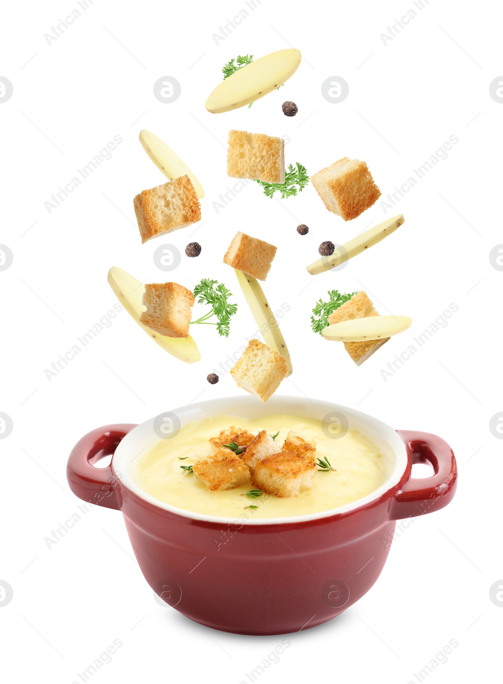 Image of Croutons and potato slices falling into bowl of soup against white background