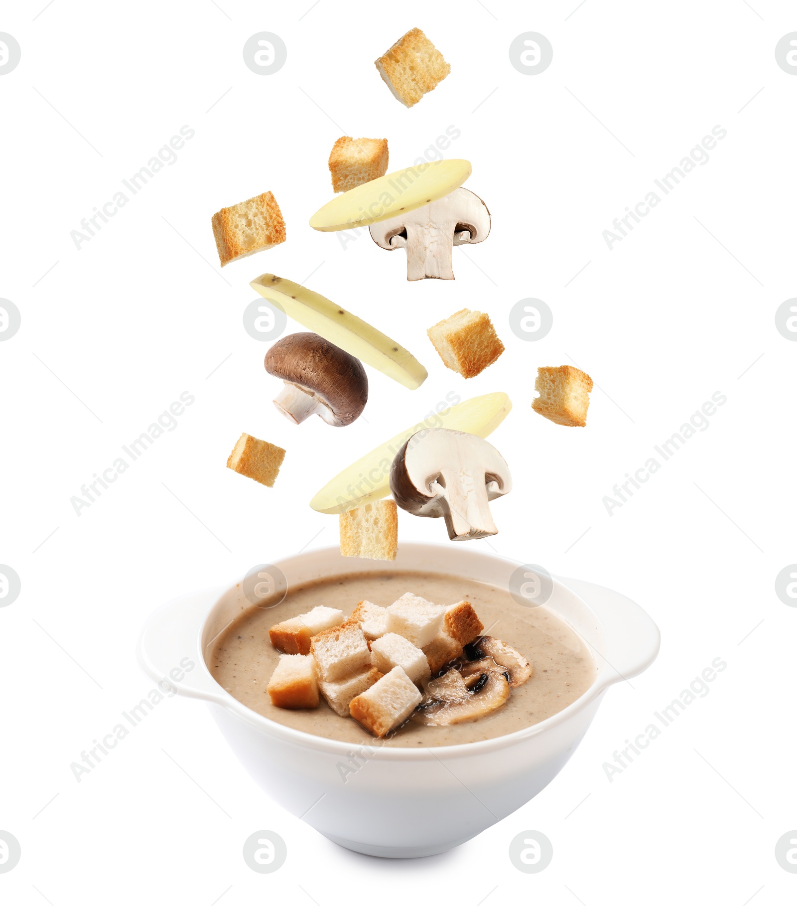 Image of Croutons, mushrooms and potato slices falling into bowl of soup against white background