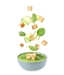 Image of Croutons, cucumber slices and basil falling into bowl of soup against white background