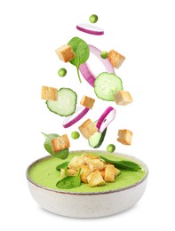 Image of Croutons, onion rings, cucumber slices and green peas falling into bowl of soup against white background