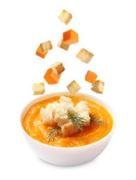 Image of Croutons and pumpkin cubes falling into bowl of soup against white background