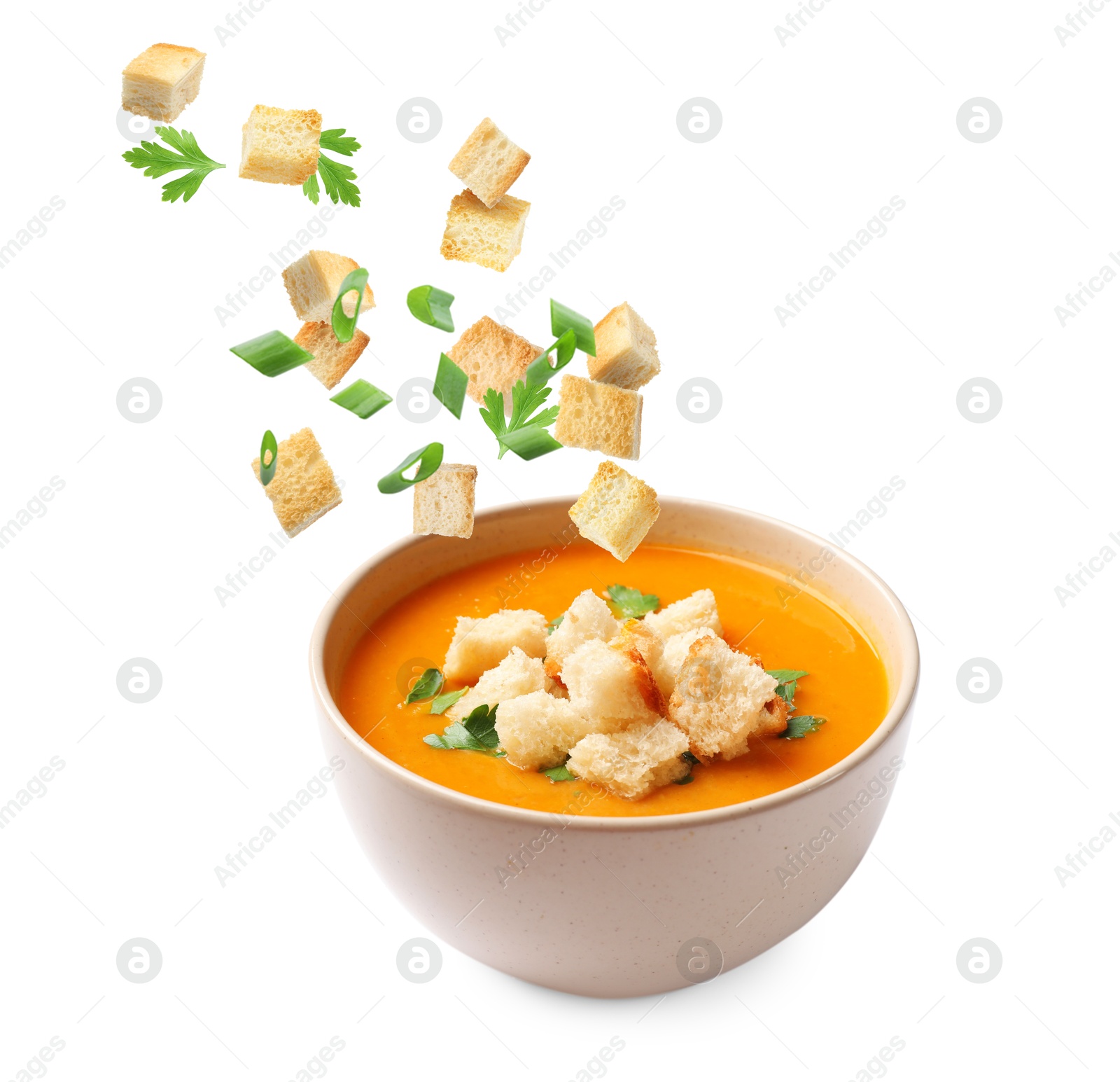 Croutons and herbs falling into bowl of soup against white background Image of Croutons and herbs falling into bowl of soup against white background