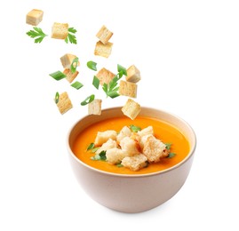 Image of Croutons and herbs falling into bowl of soup against white background