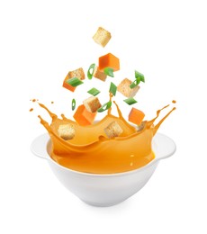 Image of Croutons and pumpkin cubes falling into bowl of soup against white background