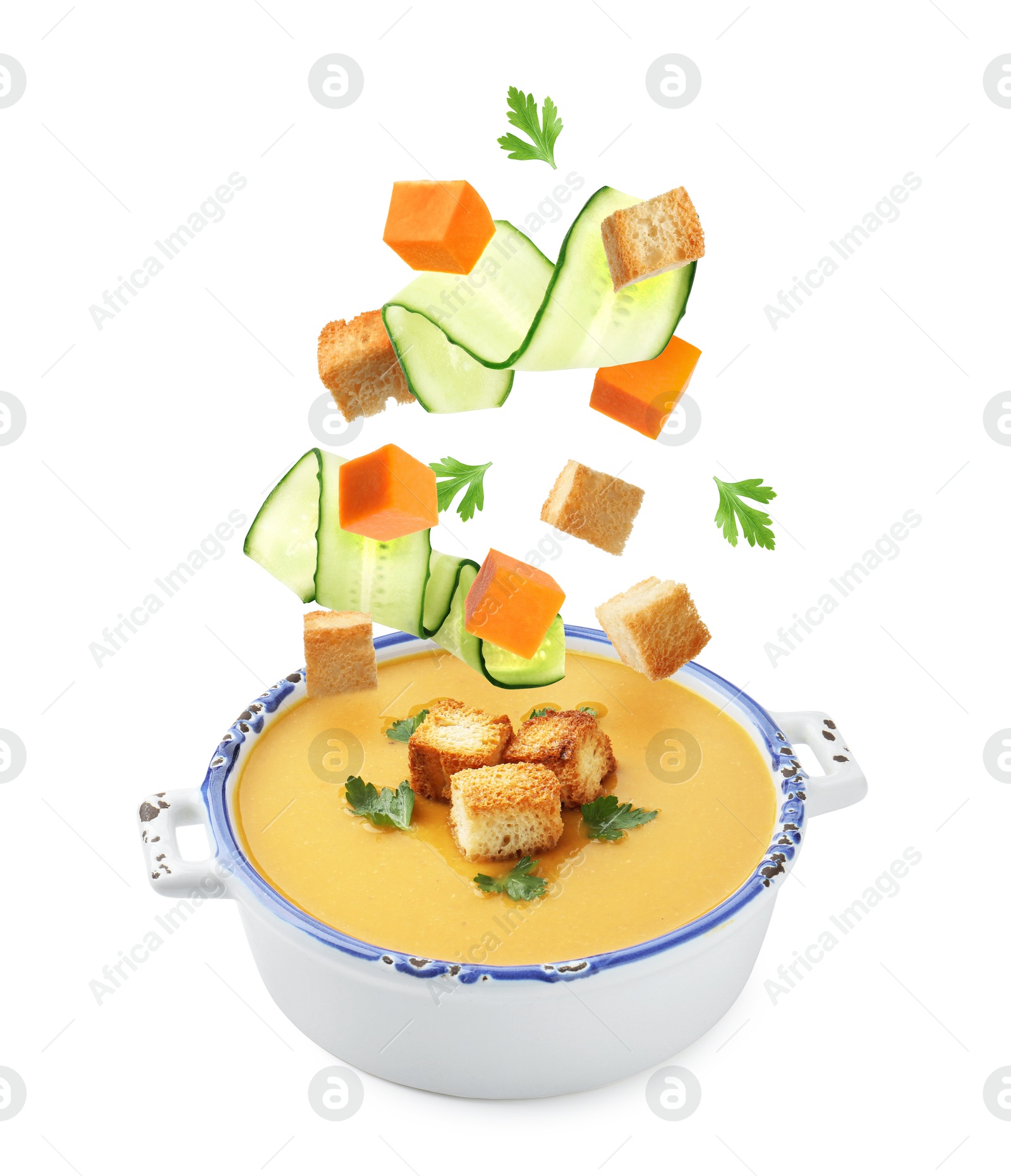 Croutons, cucumber slices and pumpkin cubes falling into bowl of soup against white background Image of Croutons, cucumber slices and pumpkin cubes falling into bowl of soup against white background