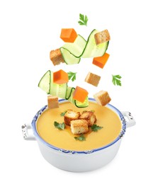 Image of Croutons, cucumber slices and pumpkin cubes falling into bowl of soup against white background