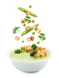 Image of Croutons and green peas falling into bowl of soup against white background