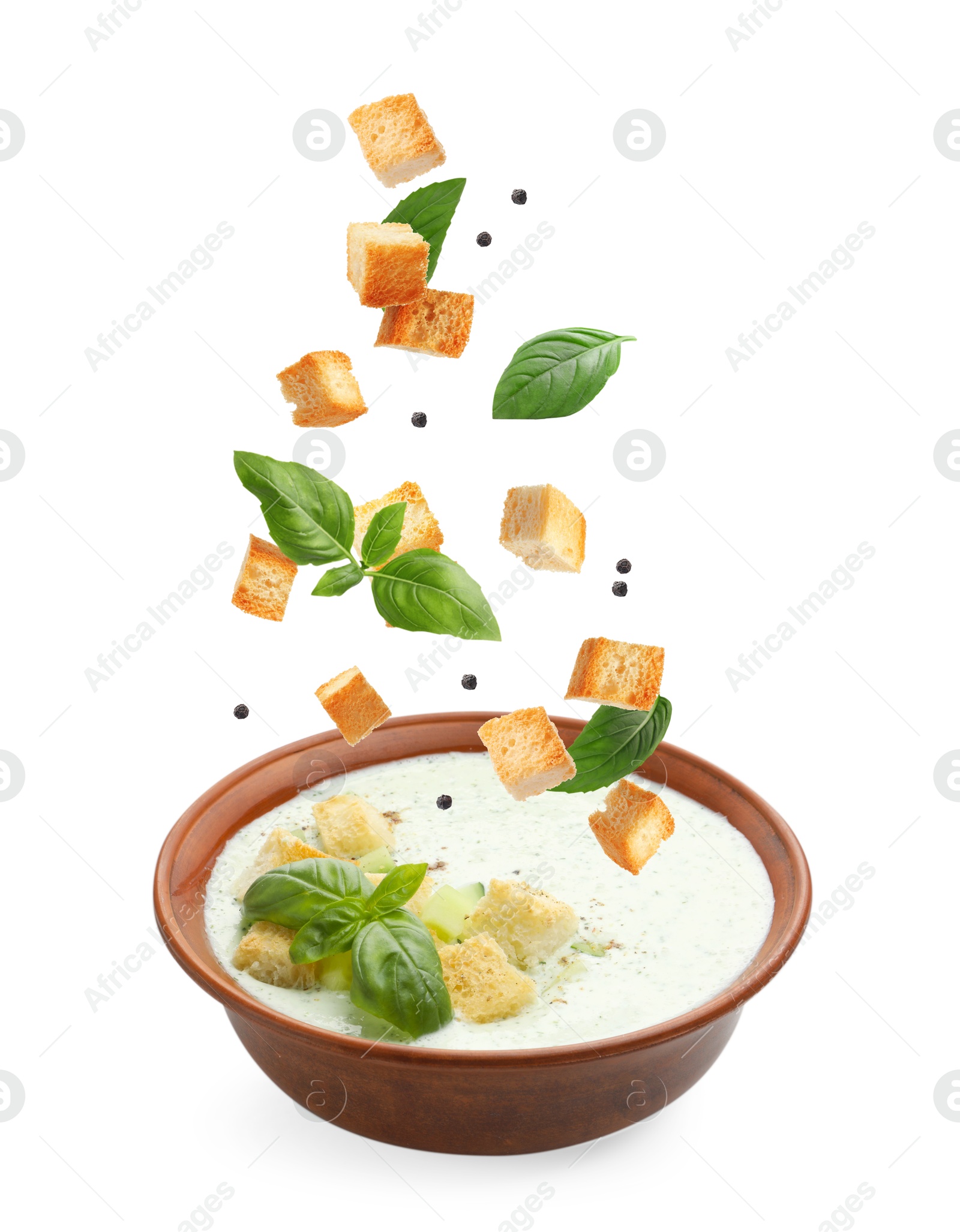 Image of Croutons and basil falling into bowl of soup against white background