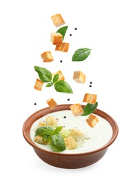 Image of Croutons and basil falling into bowl of soup against white background
