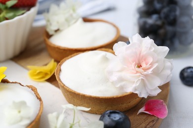 Photo of Delicious dessert. Tartlets with cream, berries and flowers on white tiled table, closeup