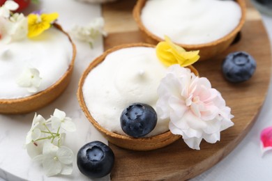 Photo of Delicious dessert. Tartlets with cream, berries and flowers on white tiled table, closeup