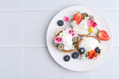 Photo of Delicious dessert. Tartlets with cream, berries and flowers on white tiled table, top view. Space for text